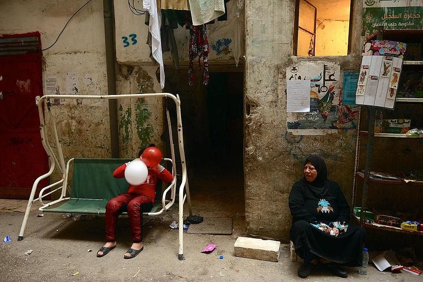 A Palestinian girl playing with balloons. Space for children to play is tight in the overcrowded camp. On the right, a refugee from Syria has set up a makeshift stall.