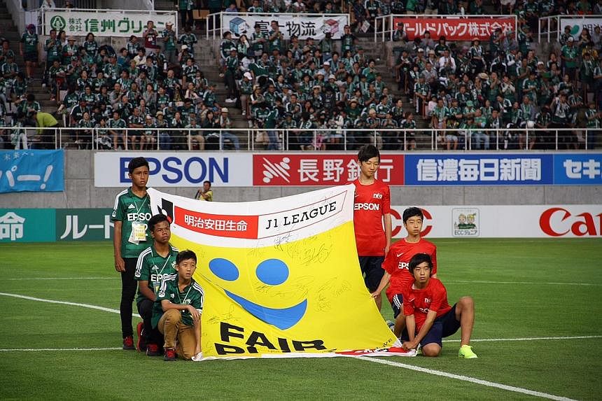 Singapore Under-14 players in green (from left) Hamizan Hisham, Nur Adam Abdullah and Elijah Lim help bring out the Fifa Fair Play flag before Yamaga's game with Shonan Bellmare.