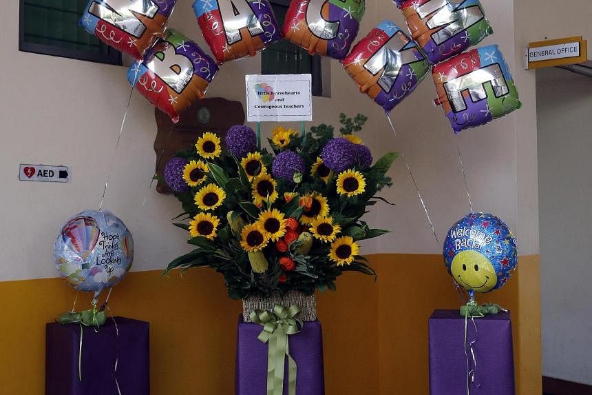 Tanjong Katong Primary School principal Caroline Wu addressing the pupils yesterday during the morning assembly, where she called on them to be strong and move on. At the entrance to the school, sunflowers and balloons (below) greeted the pupils as t