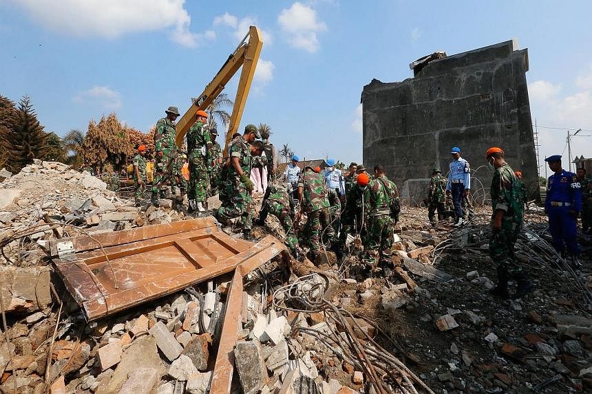 LEFT: Soldiers and police personnel clearing debris at the crash site in Medan yesterday. BELOW: Victims of the plane crash, who include relatives of soldiers and military officers, being buried in a public cemetery following a military ceremony in M