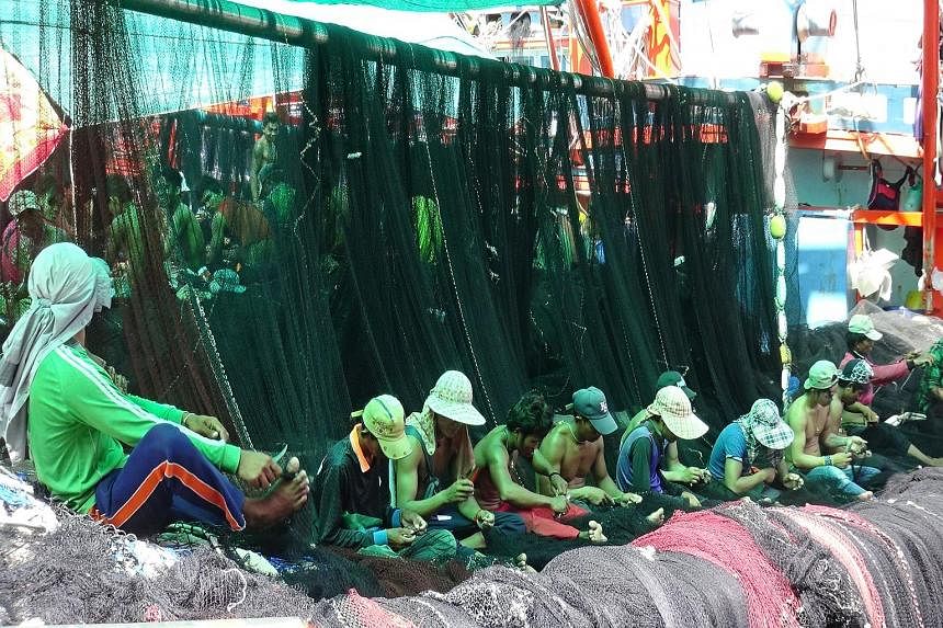 Migrant workers (above) sorting fish at a port in Mahachai, on the outskirts of Bangkok. Workers repairing fishing nets for trawlers (left) in Rayong province yesterday.