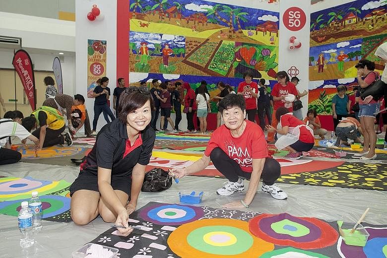 (Above) Madam Tan Wee Ling and her mother, Madam Seow Poh Gin, helping to paint a "circle of life" design yesterday at the Nanyang Community Club in Jurong West. (Below) Blocks in Jurong West displaying the residents' artworks.