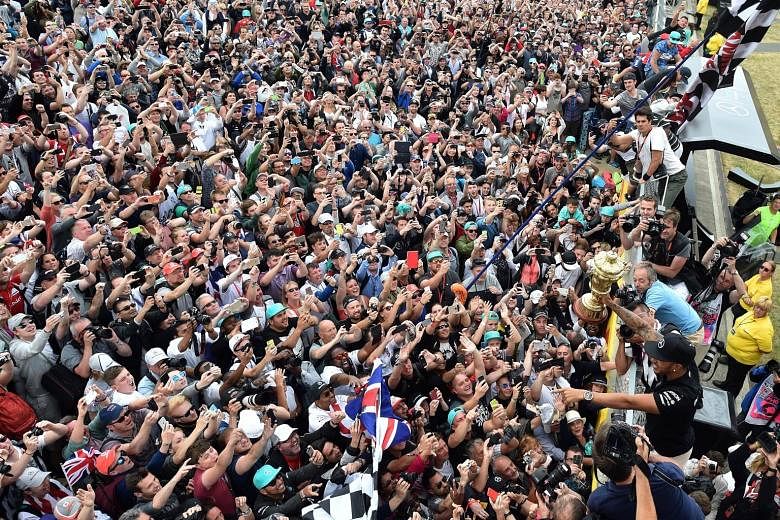 Mercedes driver Lewis Hamilton showing off his trophy to adoring home fans as he celebrates after winning the British Grand Prix for the third time at Silverstone.