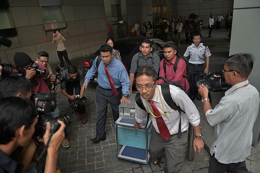 Left: Mr Najib Razak (centre), flanked by Youth and Sports Minister Khairy Jamaluddin (left) and Deputy Prime Minister Muhyiddin Yassin at an event in Putrajaya yesterday. Below: Officers seizing materials from the 1MDB office in Kuala Lumpur.