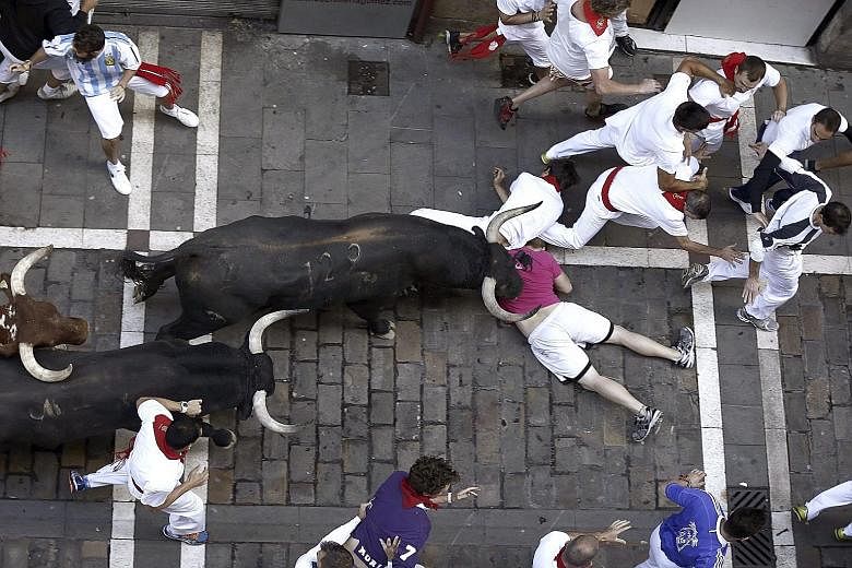 A bull running down two participants during the third bull run of the Spanish festival in Pamplona yesterday. Visitors participate in the bull runs by trying to outrun the animals along an 825m route through the narrow streets of the old city. The fe