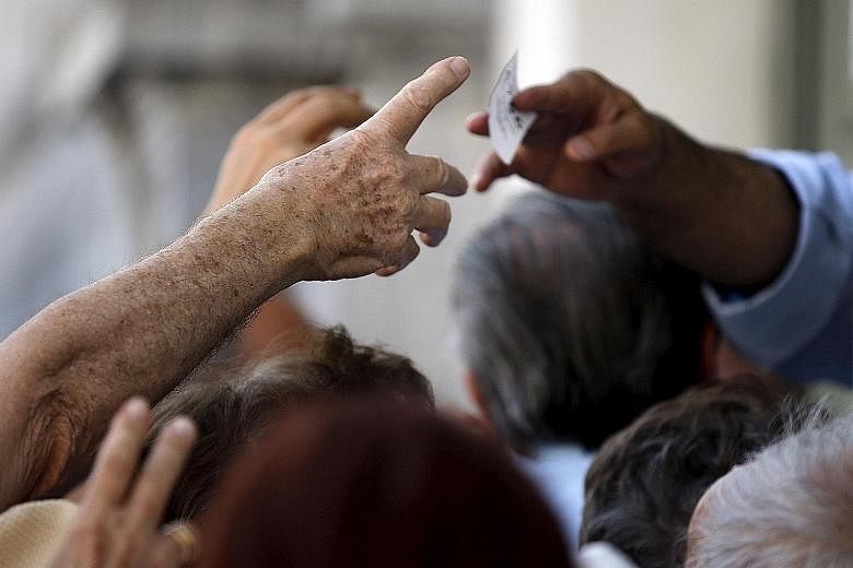 Pensioners raising their hands for priority tickets to receive part of their pensions in front of the main entrance of a National Bank branch in central Athens yesterday. ECB president Mario Draghi has characterised the Greek situation as "really dif