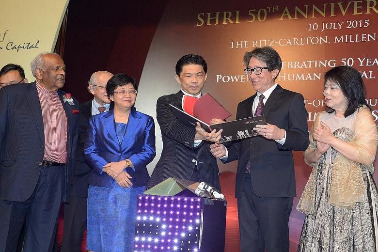 SHRI president Erman Tan showing Manpower Minister Lim Swee Say a book chronicling the institute's history. SHRI, set up in 1965, yesterday celebrated its 50th anniversary.