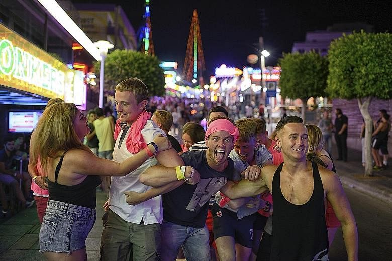 People along a neon-lit stretch of Magaluf, in Mallorca, Spain, last month. The mayor says rowdy tourist behaviour has led to a backlash among residents. Officials in popular tourist destinations from Spain to Malaysia are starting to take steps agai