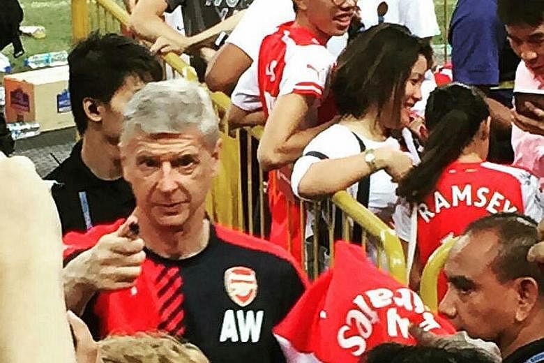Arsenal fan Joel Lam manages to snap Arsene Wenger looking in his direction, as the team's long-serving French manager signs autographs for fans at the training session held at the National Stadium.