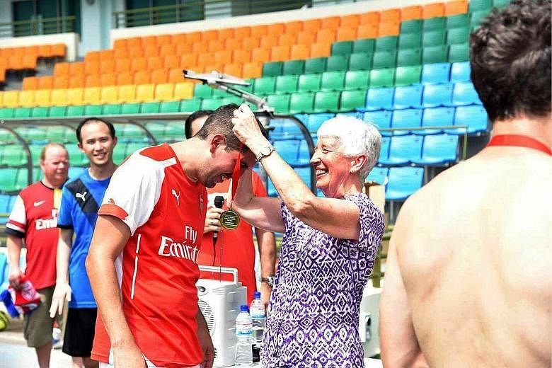 Jill Smith presenting a medal to one of the winners of a fans' football tournament organised by the Official Arsenal Singapore Supporters Club on Saturday. She helped establish more than 140 clubs worldwide.