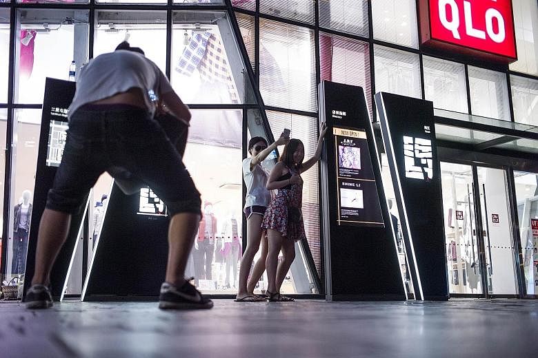People posing in front of a Uniqlo store in Beijing, after a sex video shot in a fitting room of the chain went viral. A couple and three others were held over the incident.
