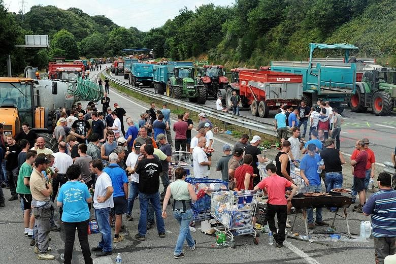 Farmers using tractors to block a highway in Quimper, north-western France, on Tuesday during a demonstration against the falling prices of their produce. Foreign competition and changing diets - people are eating less meat - have driven down pork, b
