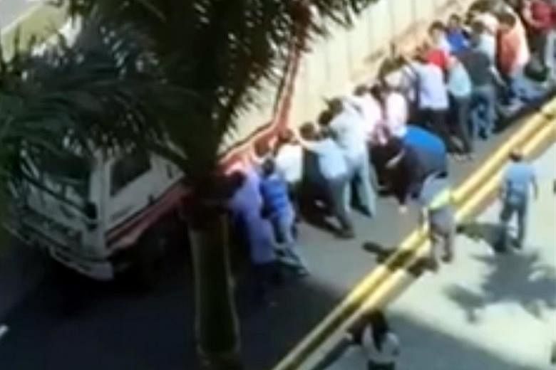 Passers-by helping to lift a lorry to free a man trapped underneath it in Boon Keng Road last Wednesday.