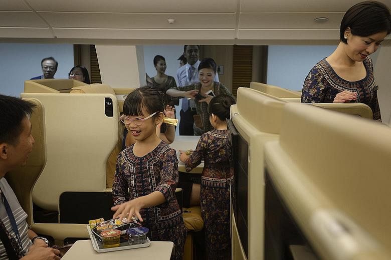"Singapore Girl" Tan Xinyu, seven, serving her dad Tan Chee Khoon, 38, an in-flight meal in a replica of Singapore Airlines' Airbus A-380 Business Class cabin yesterday at the first SIA Training Centre Open House yesterday. The event drew more than 5