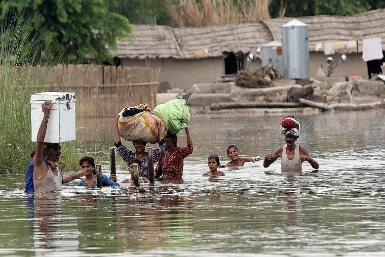 Pakistani villagers escaping rising floodwaters in Punjab province on Thursday. Elsewhere in the country, livestock and people have been swept away.