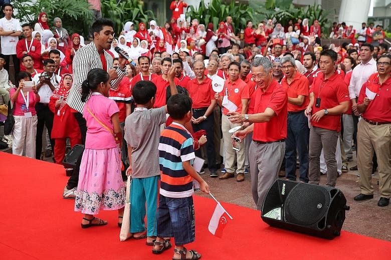 Prime Minister Lee Hsien Loong giving a Singapore flag to a child singing on stage at a National Day observance ceremony held at ITE College Central yesterday as host Shabir looked on. Also at the event were Malay MPs (behind PM Lee, from left) Senio
