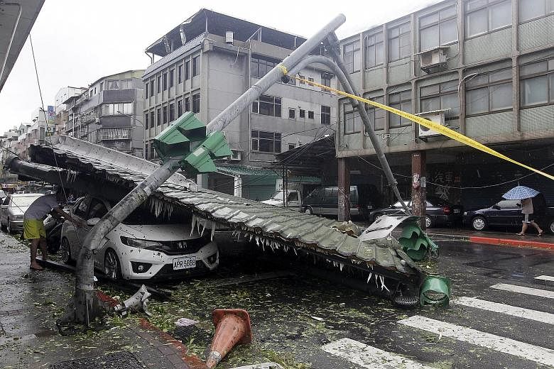 A man checking a car damaged by a fallen roof, next to a bent traffic light, in Taipei yesterday. Typhoon Soudelor's winds tore off roofs, signs and at least one bus stop from their fixtures.