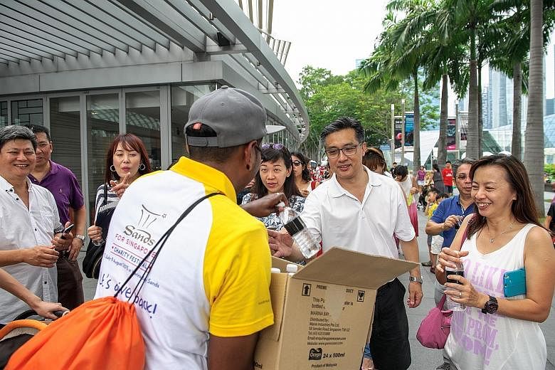 A Marina Bay Sands volunteer distributing bottled water to people lining up to visit the ArtScience Museum which offered free admission to its three exhibitions over the Golden Jubilee weekend.