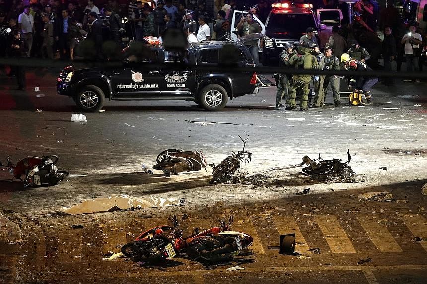 Investigators (above) at the Erawan Shrine, where blast victims were covered with white cloth. A bomb squad (below, right) investigated the nearby scene, where charred motorcycles lay on the street. Rescue workers attending to an injured person after