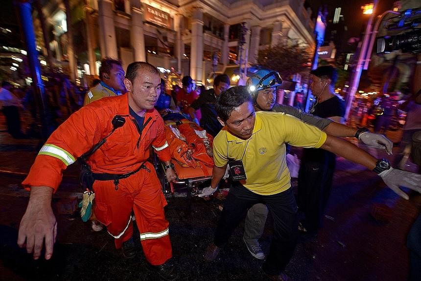 Investigators (above) at the Erawan Shrine, where blast victims were covered with white cloth. A bomb squad (below, right) investigated the nearby scene, where charred motorcycles lay on the street. Rescue workers attending to an injured person after