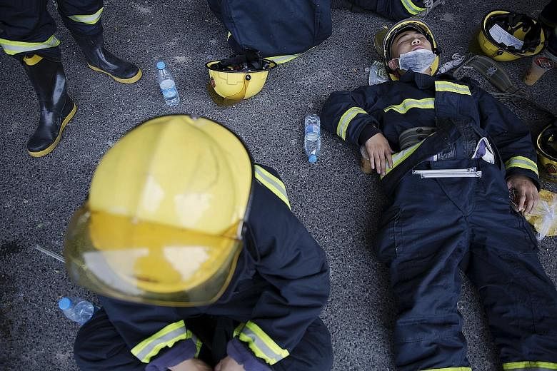 Grieving family members (above) of firefighters killed in the Tianjin blazes at a makeshift memorial yesterday. Exhausted firefighters (left) taking a break from their dangerous task trying to control the inferno.