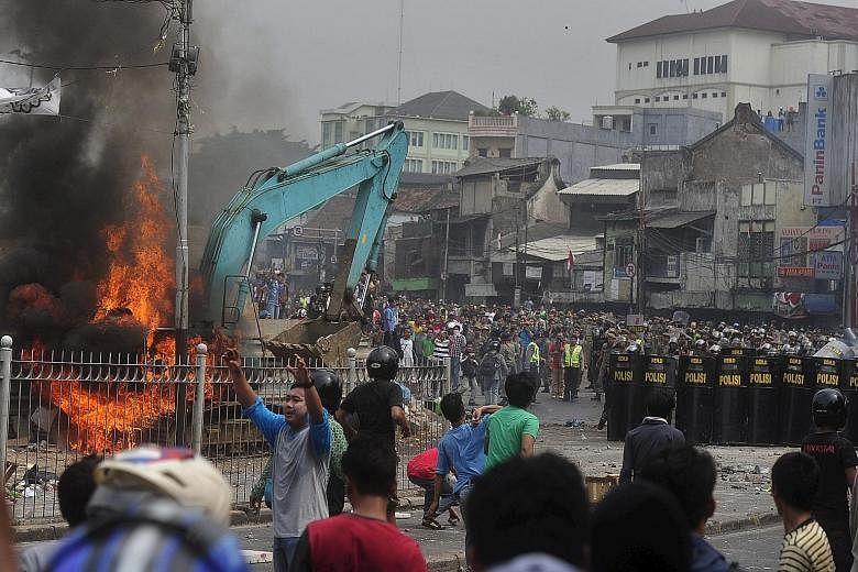 (Above) An excavator set on fire in East Jakarta yesterday during clashes in which 12 people were injured. (Below) Policemen carrying an injured resident as residents fought over the eviction of a slum in Kampung Pulo, a densely populated area on the
