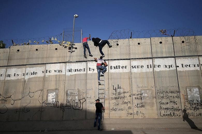 Palestinians scaling a section of the controversial barrier put up by Israel. When the Berlin Wall was torn down a quarter-century ago, there were 16 border fences worldwide. Today, it is said that there are 65 such barriers, either completed or unde
