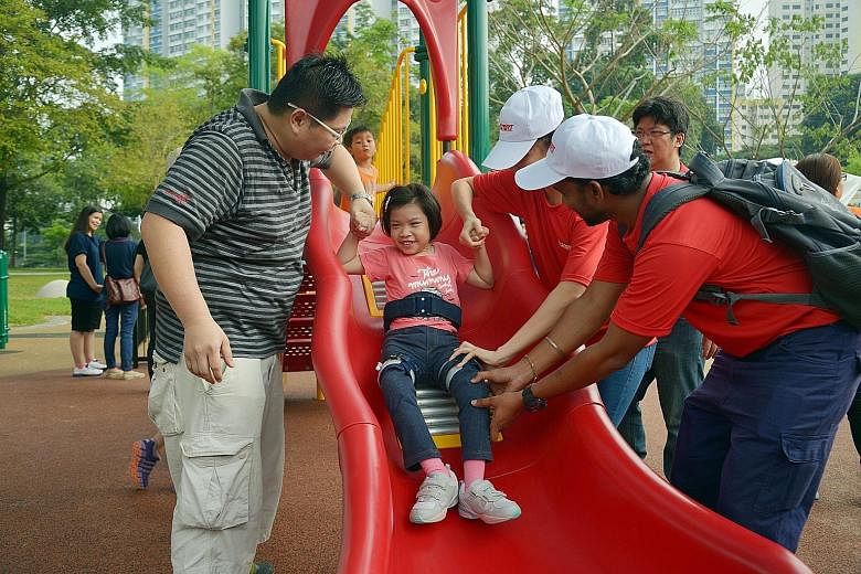 Fong Ruo En (above), six, trying out the special-needs friendly slide, which has rollers to stimulate the sense of touch and ease friction. Meanwhile, Minister Tan Chuan-Jin (right) gives the merry-go-round a good push, to the delight of a little gir