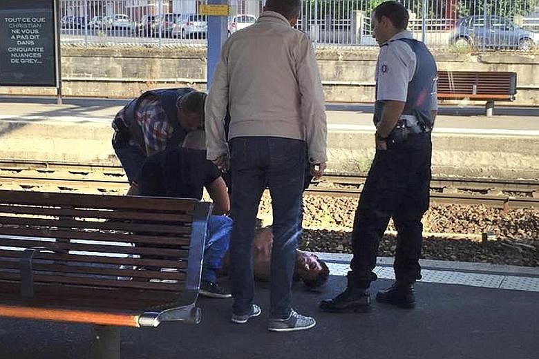 French police (left) standing over a man who was apprehended on the platform at the Arras train station (above) in France after a man opened fire on a high-speed train.