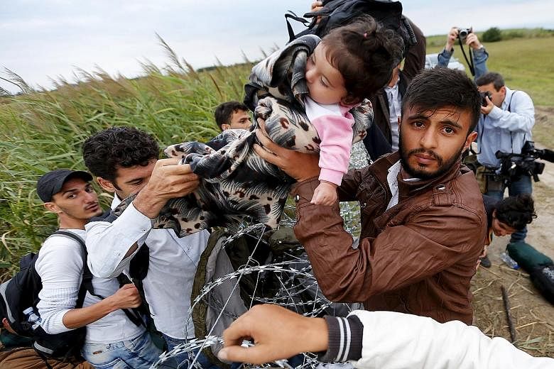 A child being handed across a barbed wire fence as Syrian migrants try to enter Hungary from areas near the country's border with Serbia.