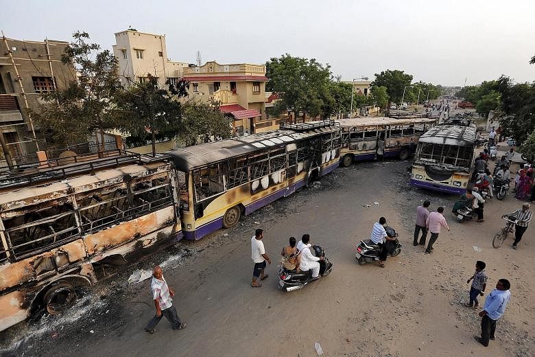 Burned buses line a street in Ahmedabad after clashes between the police and protesters in the past two days left at least nine people dead.