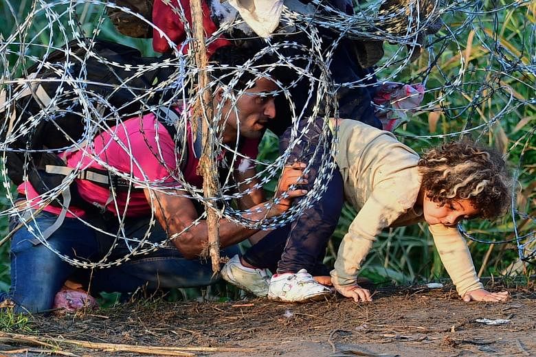 A migrant family creep under a barbed fence at the Hungarian-Serbian border. Some experts believe the term "migrant" is no longer a fitting word to use to describe the horror unfolding in the Mediterranean.