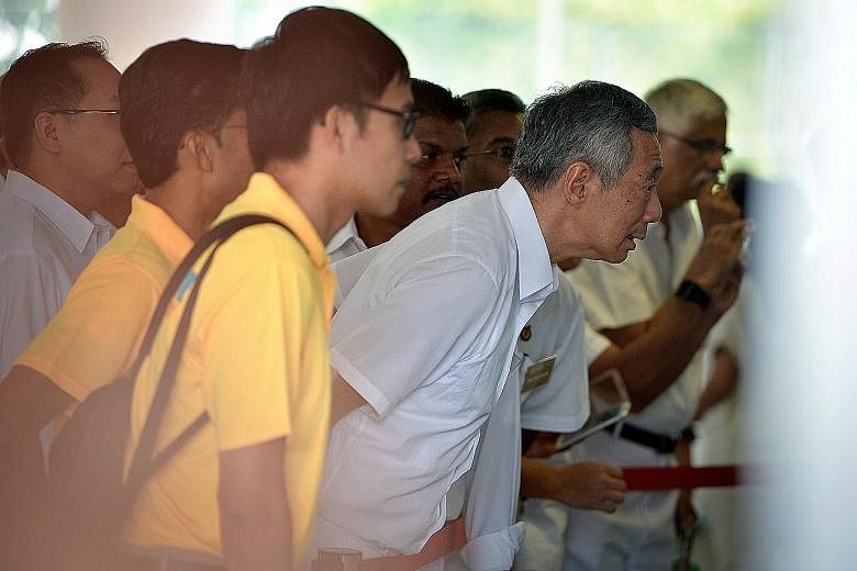PM Lee Hsien Loong (left) and activist Roy Ngerng (with bag) checking the nomination papers outside the RI school hall yesterday. PM Lee will lead the PAP team against Mr Ngerng's Reform Party in Ang Mo Kio GRC.