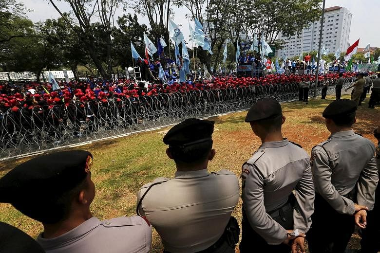 Trade union supporters standing behind razor wire in front of the Presidential Palace in Jakarta yesterday. Thousands of workers protested against job cuts and called for higher wages, raising pressure on the government as it struggles to kick-start 