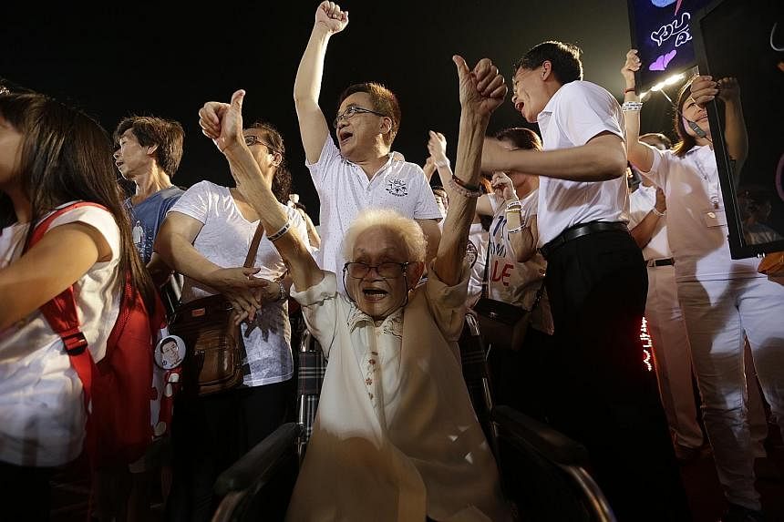 Above: Bedok resident Quek Jee Yee, 84, cheering along with Transport Minister Lui Tuck Yew (right) at the People's Action Party rally at Bedok Stadium yesterday. Right: A Workers' Party supporter holding up a "hammer", the symbol of the opposition p