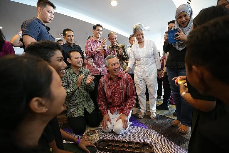 PM Lee Hsien Loong playing an improvised game of congkak integrated with language and culture with students from Orchid Park Secondary School, while his wife Ho Ching and Mr Zaqy Mohamad (next to him) look on. Mr Lee was attending the launch of Malay