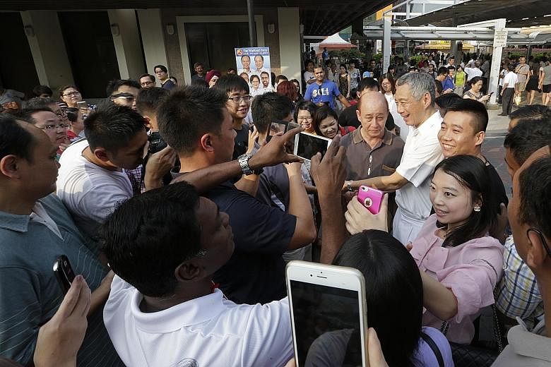 Prime Minister Lee Hsien Loong surrounded by people wanting to have photographs taken with him outside Hougang MRT station during a walkabout with the PAP candidates for Aljunied GRC yesterday.