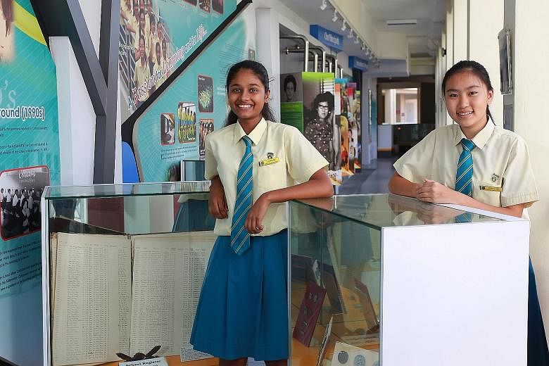 Secondary 3 students S. Darshana (left) and Estella Tan at their school's heritage gallery. Among the items on display are old photos, a handwritten register of students' names and their family details that was used in the 1950s and 1960s, and old sc