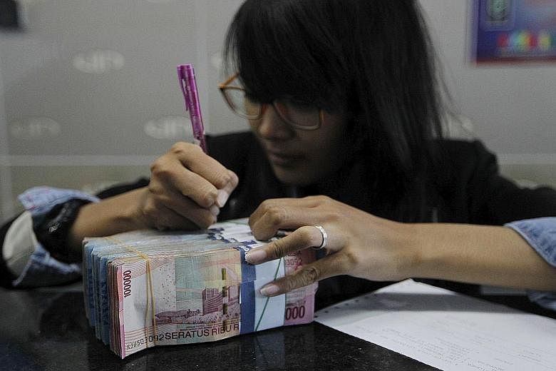 A money changer handling notes in Jakarta. The rupiah has slid 4.9 per cent since July, less than half the 11 per cent slide in the ringgit.