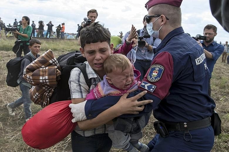 A Hungarian policeman attempting to stop a migrant child carrying a baby from running away from a collection point in Roszke, Hungary, on Tuesday. At least 400 desperate migrants have broken through police lines at the flashpoint town. Migrants yeste
