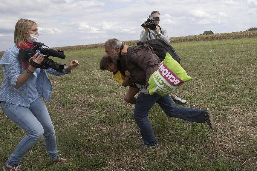 A migrant with a child (above) running away before being tripped (right) by the TV camerawoman filming them in a Hungarian village this week.