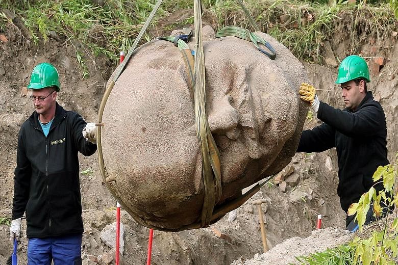 Workers moving a giant granite head of Russian revolutionary leader Vladimir Lenin in a forest in Berlin, Germany, on Thursday. The head of the Lenin monument, which was dismantled in 1991, had been long buried and half forgotten in the forest in the