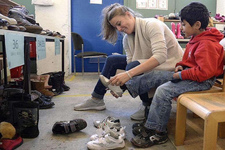 A volunteer helper putting on a shoe for a Syrian boy at a refugee centre in Munich. Thousands of Germans have joined its biggest post-war refugee relief by handing out essentials, giving German lessons and opening up their homes, among other things.