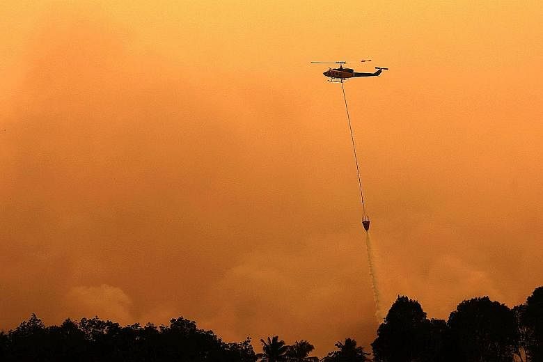 A helicopter dropping water to extinguish a raging fire in Ogan Komering Ilir, in Indonesia's South Sumatra province, on Sunday. Above: An aerial view of smoke rising from a burning forest in Ogan Komering Ulu last Thursday. Left: A worker donning pr