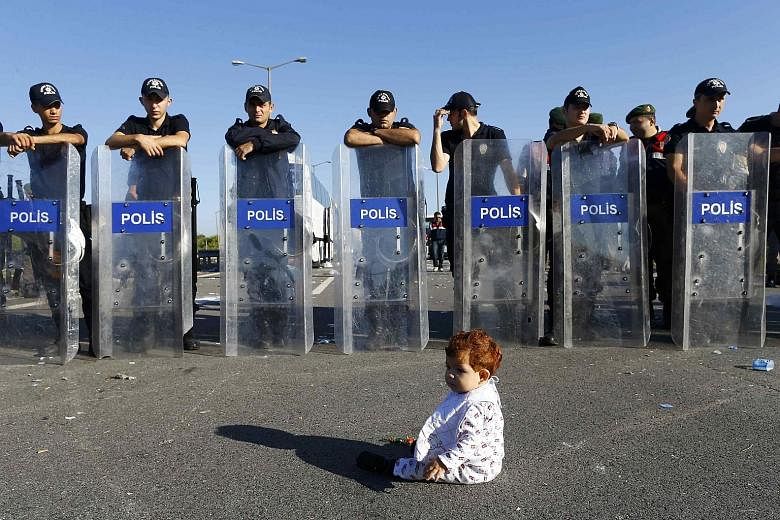 An infant sitting on the road in front of a line of Turkish policemen blocking migrants on a highway near Edirne yesterday. Older, unaccompanied children seeking asylum in Europe suffer different fates. They are looked after in Sweden but in other co