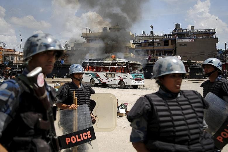 Members of the Nepalese Armed Police Force in front of a bus set on fire by protesters in Kathmandu yesterday. Weeks of clashes with the police over the new Constitution have left more than 40 people dead.