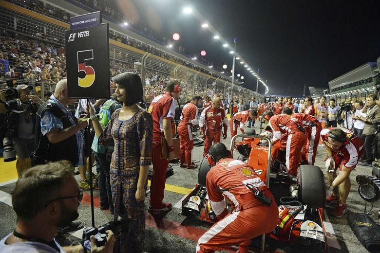 A Singapore Girl holding up Sebastian Vettel’s pole position placard as the teams get ready for the start. 