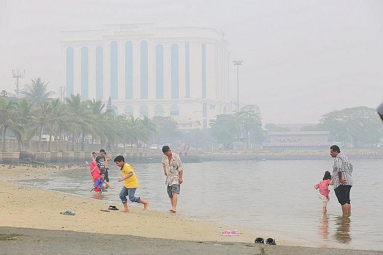 MALAYSIA: People having a dip at Stulang in Johor Baru during the holiday yesterday despite the haze which partly obscured the Berjaya Waterfront Hotel in the background. INDONESIA: (Above) Soldiers surveying burnt peat land during President Joko Wid