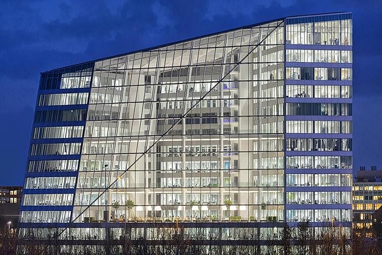 From the outside (left), the Edge building in Amsterdam looks as if a wedge has been sliced off the building. Inside (below), about 2,500 Deloitte workers share 1,000 desks, which are used only when they are needed. The building, rated the greenest i