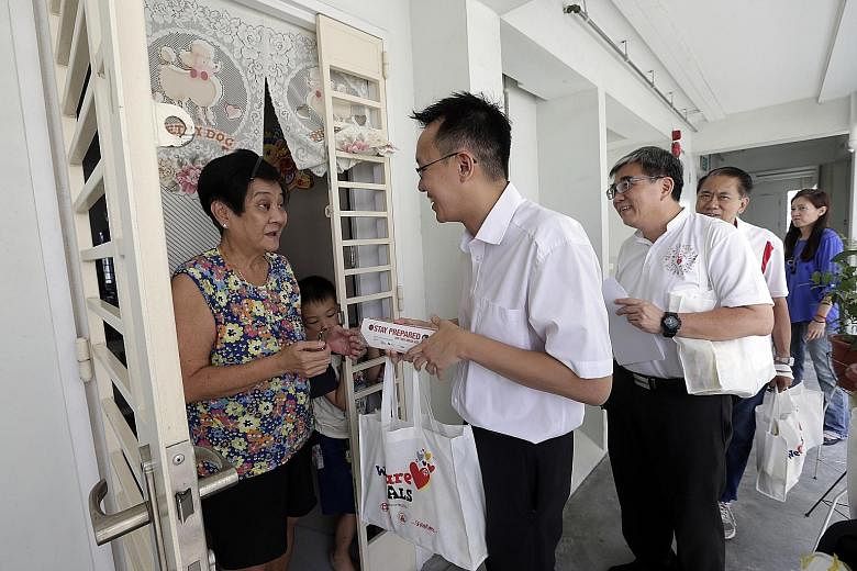 Madam Chua Geok Keow, 65, and grandson Louis Lim, seven, receiving a WeCare pack from Jurong GRC MP Tan Wu Meng and grassroots volunteers in Clementi yesterday. The pack has items such as N95 masks and instant noodles.